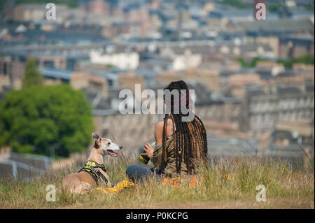 Eine sehr kühle, böhmische Mädchen sitzt in der langen Gras auf Carlton Hill an einem sonnigen Tag mit Edinburgh unter ihr und ihrem Hund Stockfoto