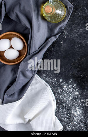 Blick von oben auf die rohe Eier in der Schale, eine Flasche Öl und Mehl auf dunklem Marmor Oberfläche Stockfoto