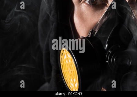 Mann in Schwarz Haube durch das Tragen von schützender Maske durch Rauchwolken umgeben Stockfoto