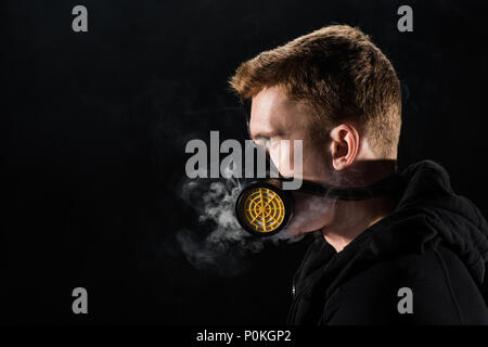 Mann in Schwarz Haube durch das Tragen von schützender Maske durch Rauchwolken umgeben Stockfoto