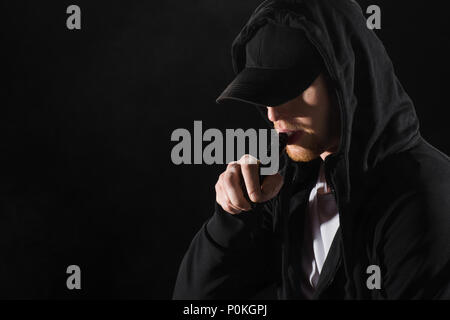 Junge bärtige Mann mit Kappe rauchen Elektronische Zigarette isoliert auf Schwarz Stockfoto