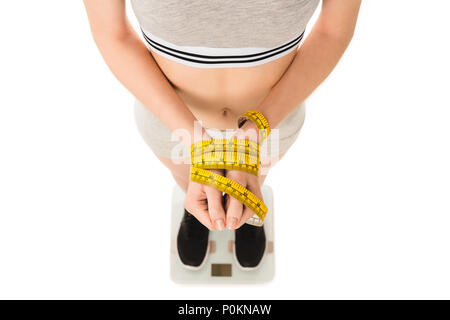 7/8 shot der jungen Frau mit gebundenen Händen mit Maßband stehen auf Skalen, die isoliert auf weißem Stockfoto