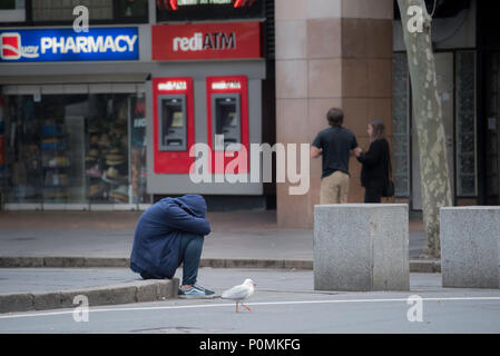 Eine Person allein und sitzt auf einem Fußweg Edge mit dem Kopf nach unten und in die Knie zu zwingen, in die Stadt Sydney mit anderen Menschen begraben vorbei gehen. Stockfoto
