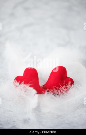 Zwei rote Herzen liegen auf weißen Flaum. Metapher der Liebe. Grußkarten zum Valentinstag. Bild vertikal Stockfoto