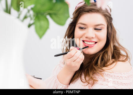 Portrait von lächelnden jungen Frau Anwendung Lip Gloss während Make-up zu Hause Stockfoto