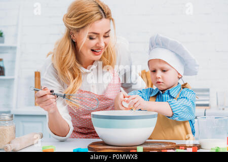 Lächelnde Mutter mit der Hand der Auswurftrommel und dem kleinen Jungen in die Schüssel gießen Ei Stockfoto