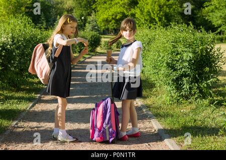 Ansicht der Rückseite zwei Schulmädchen Freundinnen mit Rucksäcken Eis essen. Stockfoto