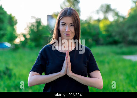 Schöne junge Mädchen im Sommer im Park auf Urlaub. Eine Geste zeigt das Gebet mit seinen Händen. Glücklich lächelnd. Er sieht sie genau auf den Rahmen. Gefühl der Demut. Stockfoto