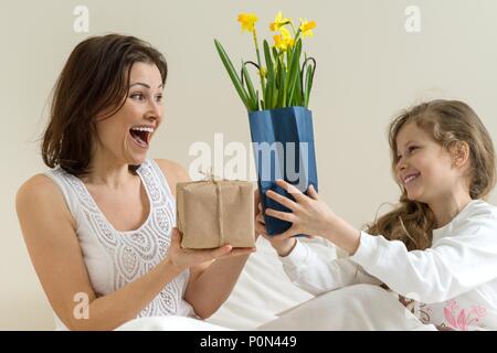 Muttertag. Die kleine Tochter hält ein Geschenk und Blumen für Ihre Mutter. Hintergrund Interieur der Zimmer, der Mutter im Bett, morgen Stockfoto