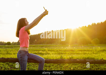 Outdoor portrait einer jungen Teenager Mädchen mit einem Smartphone für Ihren Blog, und Seiten sozialer Netzwerke. Selfie bei Sonnenuntergang. Stockfoto