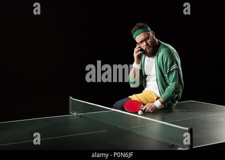 Tennis Player sprechen auf dem Smartphone beim Sitzen auf Tischtennis isoliert auf Schwarz Stockfoto