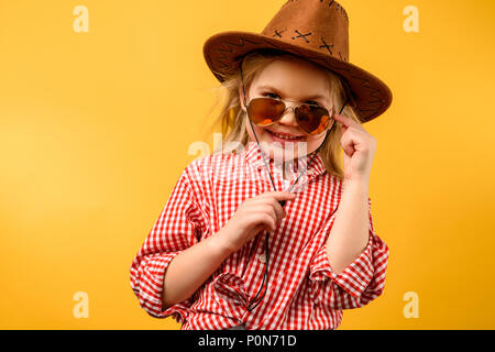 Stilvolle cowgirl in Hut und Sonnenbrille, isoliert auf Gelb Stockfoto