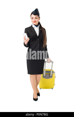 Junge Stewardess mit Koffer an Smartphone isoliert auf weißem suchen Stockfoto