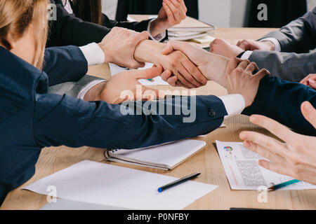 Zugeschnittenes Bild von zwei Geschäftspartnern die Hände schütteln, während Geschäftsfrau ihre Hände halten am Tisch im Büro Stockfoto