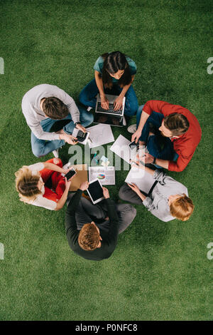 Ansicht von oben der Geschäftsleute arbeiten mit Geräten und Dokumenten, die auf Gras Stockfoto