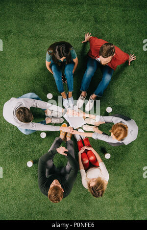 Ansicht von oben von Geschäftspartnern halten sich an den Händen und sitzen mit einem anderen Kollegen auf Gras Stockfoto