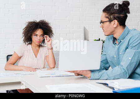 Geschäftsmann etwas auf Laptop amerikanischen Geschäftsfrau im Amt zu afrikanischen Stockfoto