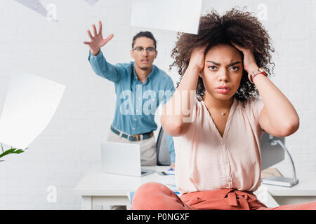 Geschäftsfrau leiden unter Kopfschmerzen, während ihre männlichen Kollegen im Büro schreien Stockfoto