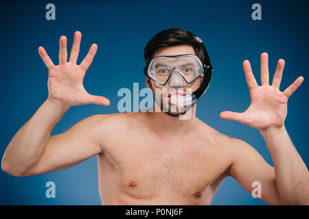Fröhlicher junger Mann in Schnorchel und Taucherbrille gestikulierte mit Händen und Kamera auf Blau Stockfoto