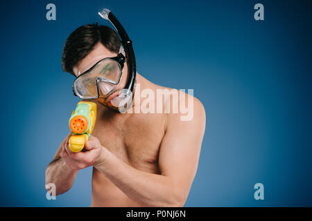 Junger Mann in Schnorchel und Taucherbrille holding Wasserpistole auf Blau Stockfoto