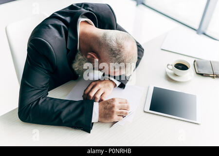 Blick von oben auf die Überforderten älteren Geschäftsmann schlafen am Arbeitsplatz mit Büromaterial Stockfoto