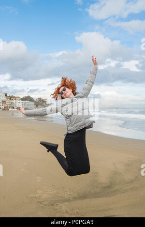 Glückliche junge Frau springen auf Seashore an bewölkten Tag, Anzio, Italien Stockfoto