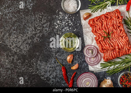Rohes Hackfleisch auf Papier mit Zwiebeln, Kräutern und Gewürzen auf schwarzem Hintergrund, Ansicht von oben. Stockfoto