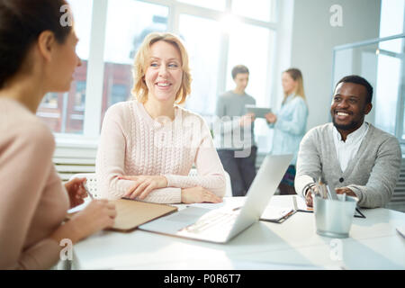 Fröhliches Team der weißen Arbeiter Spaß zusammen, während im ehrgeizigen Projekt Diskussion gewickelt, Interieur des Großraumbüro auf Hintergrund Stockfoto