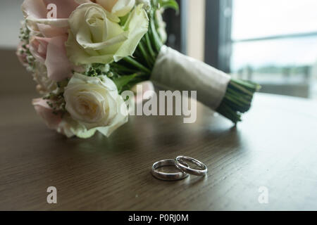 Schöne getonten Bild mit Hochzeit Ringe liegen auf einem Holztisch einen Blumenstrauß im Hintergrund Stockfoto