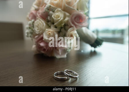 Schöne getonten Bild mit Hochzeit Ringe liegen auf einem Holztisch einen Blumenstrauß im Hintergrund Stockfoto