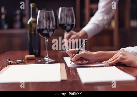 Zwei Sommeliers, männlichen und weiblichen Weinprobe Rotwein und sich Notizen auf degustation Karte Stockfoto