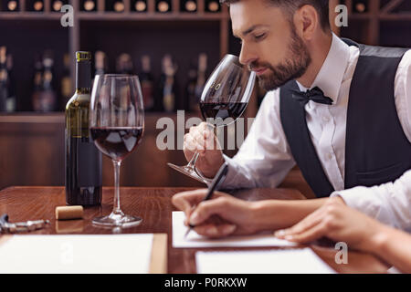 Zwei Sommeliers, männlichen und weiblichen Weinprobe Rotwein und sich Notizen auf degustation Karte Stockfoto