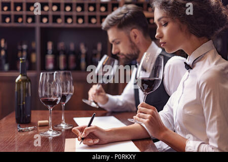 Zwei Sommeliers, männlichen und weiblichen Weinprobe Rotwein und sich Notizen auf degustation Karte Stockfoto