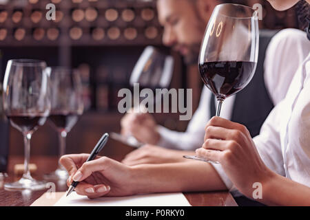 Zwei Sommeliers, männlichen und weiblichen Weinprobe Rotwein und sich Notizen auf degustation Karte Stockfoto