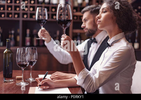 Zwei Sommeliers, männlichen und weiblichen Weinprobe Rotwein und sich Notizen auf degustation Karte Stockfoto