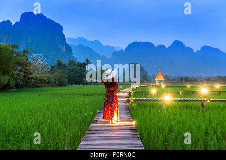 Junge Frau zu Fuß auf Holz- Pfad mit grünen Reisfeldern in Vang Vieng, Laos. Stockfoto