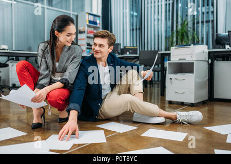 Junge glücklich Geschäftspartner Schreibarbeit zu tun, während auf dem Boden im Büro sitzen Stockfoto