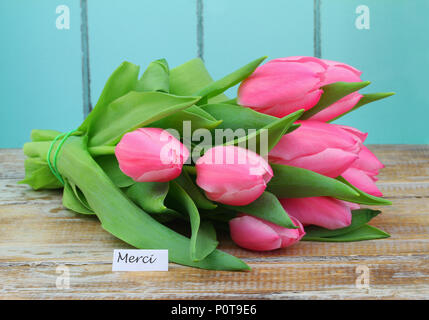 Merci (vielen Dank, dass Sie sich in Französisch) Karte mit rosa Tulpe Strauß auf Holzmöbeln im Landhausstil Oberfläche Stockfoto