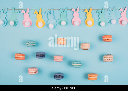 Blick von oben auf die Ostern Kaninchen Garland und bunte Macarons auf der blauen Fläche Stockfoto