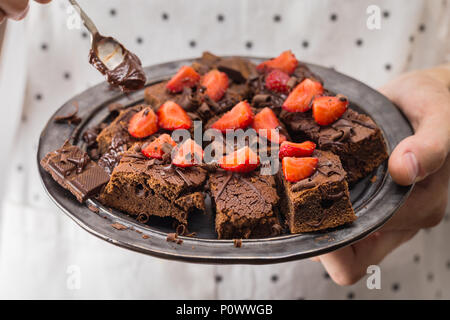 Mann kochen Halteplatte mit leckeren Chocolate brownies, Schokoladensauce und Erdbeeren. Nahaufnahme Stockfoto