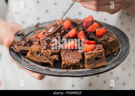 Mann kochen Halteplatte mit leckeren Chocolate brownies, Schokoladensauce und Erdbeeren. Nahaufnahme Stockfoto