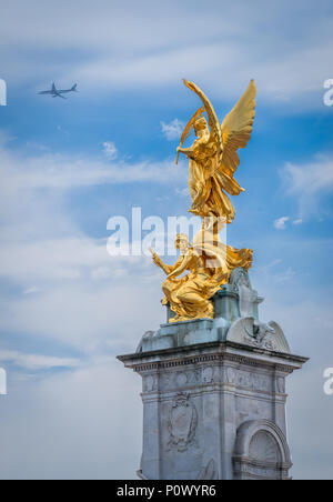 Ein Passagier Jet fliegt vorbei an der Queen Victoria Memorial, die Geflügelten Sieg Skulptur auf aussieht. Stockfoto