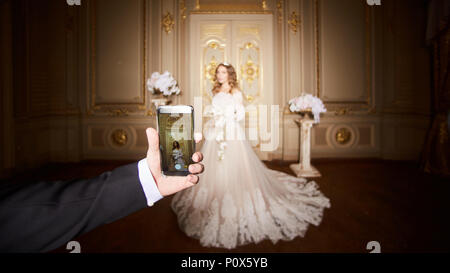 Fotografieren einer Braut durch das Smartphone im luxuriösen Innenraum im barocken Stil. Stockfoto
