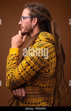 Junge schöne Hispanic Mann mit Dreadlocks gegen Braun backgr Stockfoto