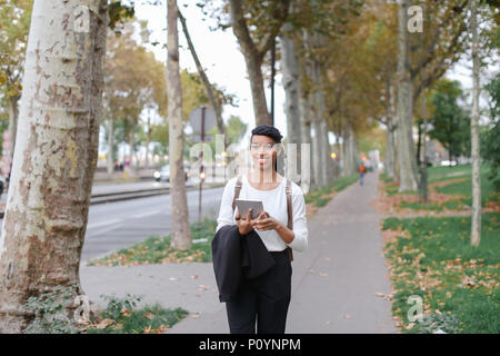 Schöne schwarze Studentin zu Fuß nach Klassen mit Tablet auf der Straße mit Laub. Stockfoto