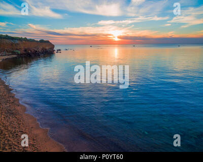 Sonnenuntergang über ruhige Meer Wasser in der Nähe der zerklüfteten Steilküste Stockfoto