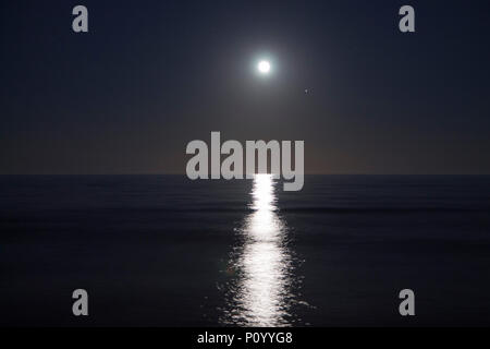Große Vollmond steigt über dem Meer in der Nacht. Lunar reflektierte Licht auf dem Wasser. Lunar weg. Ozean. Stockfoto