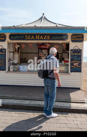 Ein Mann schaut auf einen Fischhändler Stall direkt an der Küste am Strand von Brighton, East Sussex. Marktstand an der Promenade am Strand von Brighton. Stockfoto