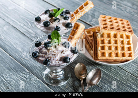 Quark Dessert mit Blaubeeren in einem Glas Schale und hausgemachten Wiener Waffeln auf einem hölzernen Hintergrund Stockfoto