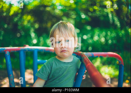 Ein süßer kleiner Junge sitzt auf einem Karussell im Park Stockfoto